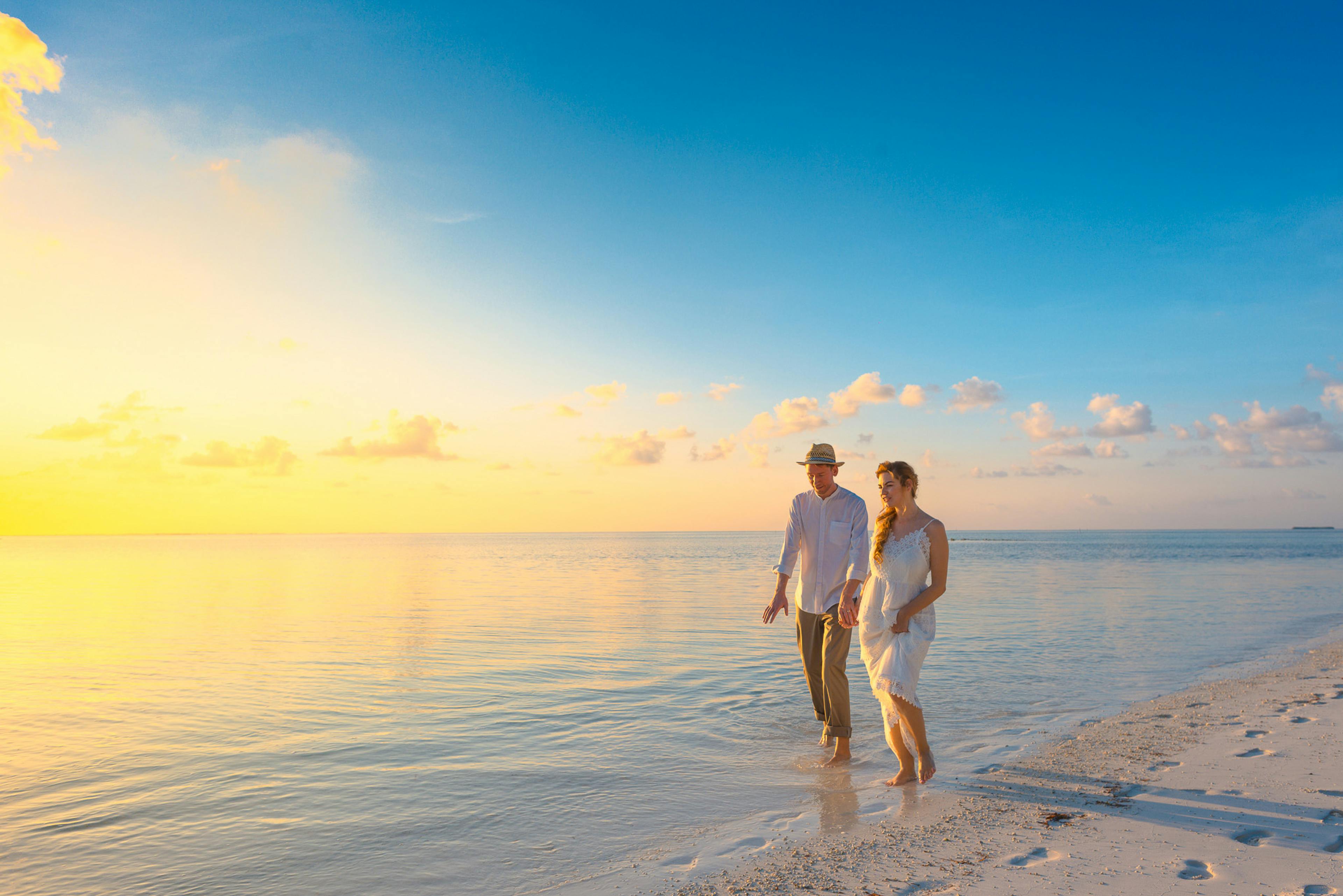 A couple walks hand in hand along a golden Maldivian shoreline at sunset