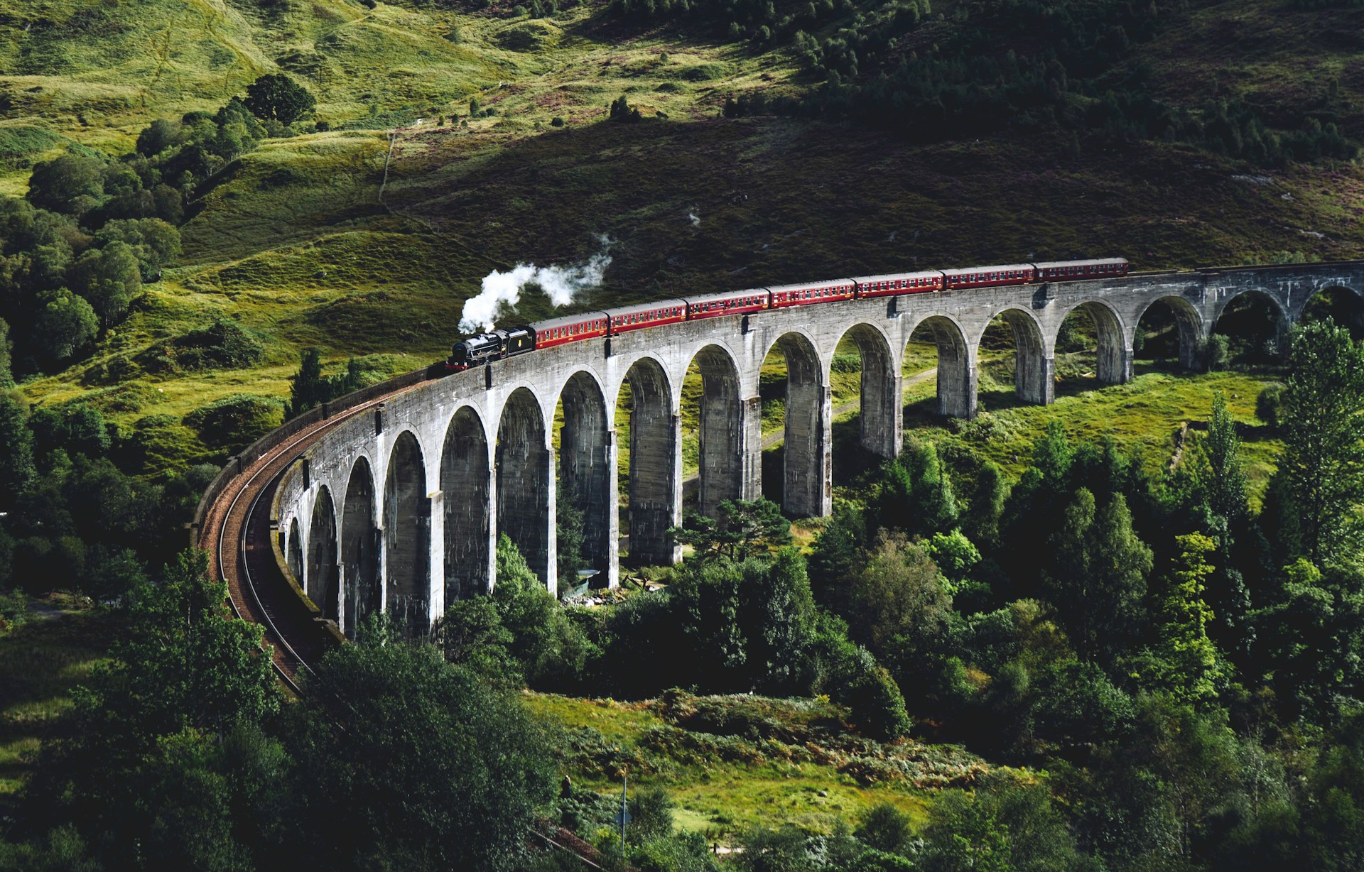 A train traversing the majestic Glenfinnan Viaduct with the lush Scottish Highlands in the background.