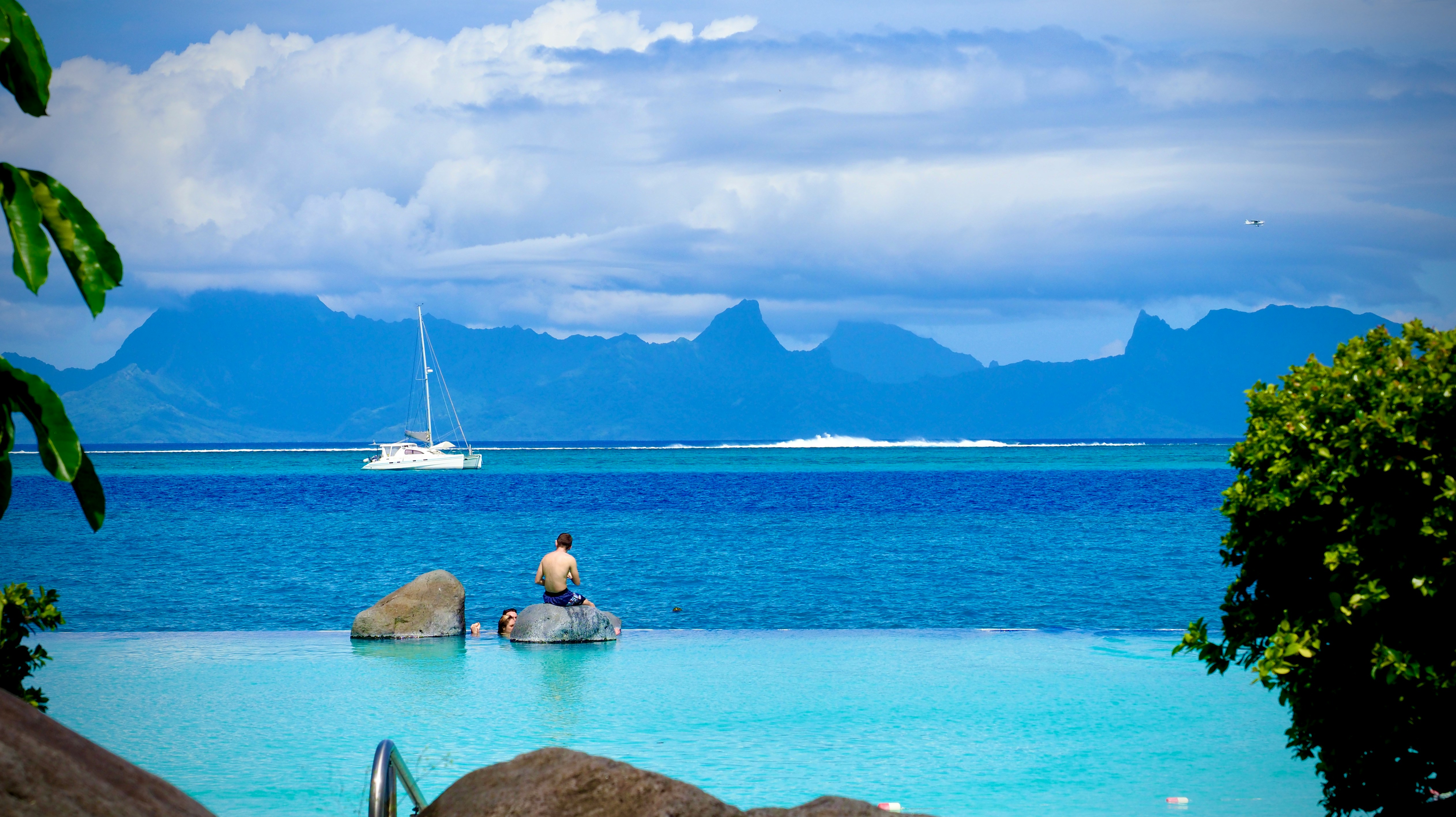 Two people and a white sailboat in Tahiti’s deep blue ocean