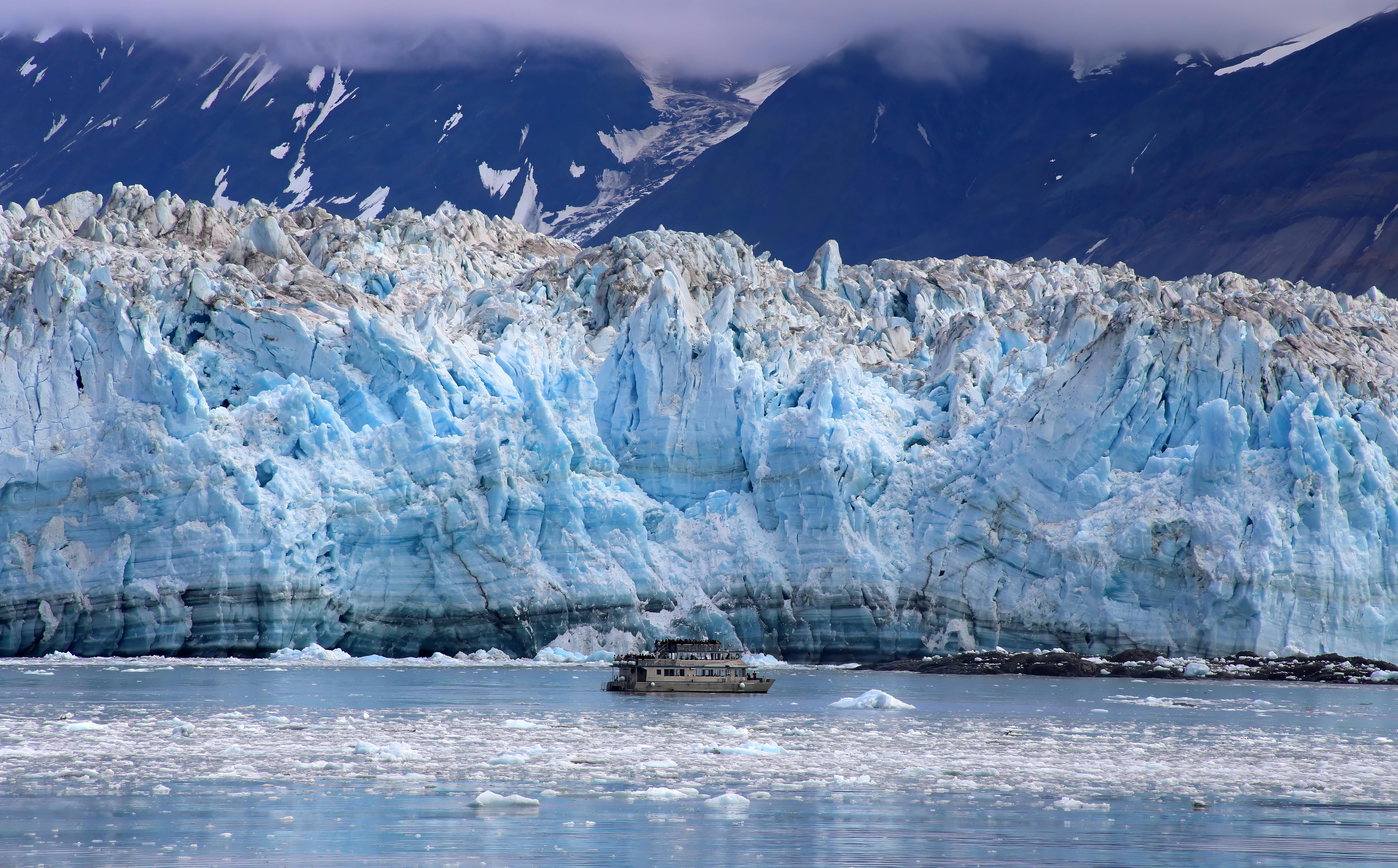 A small cruise ship drifts near the towering blue ice of Hubbard Glacier