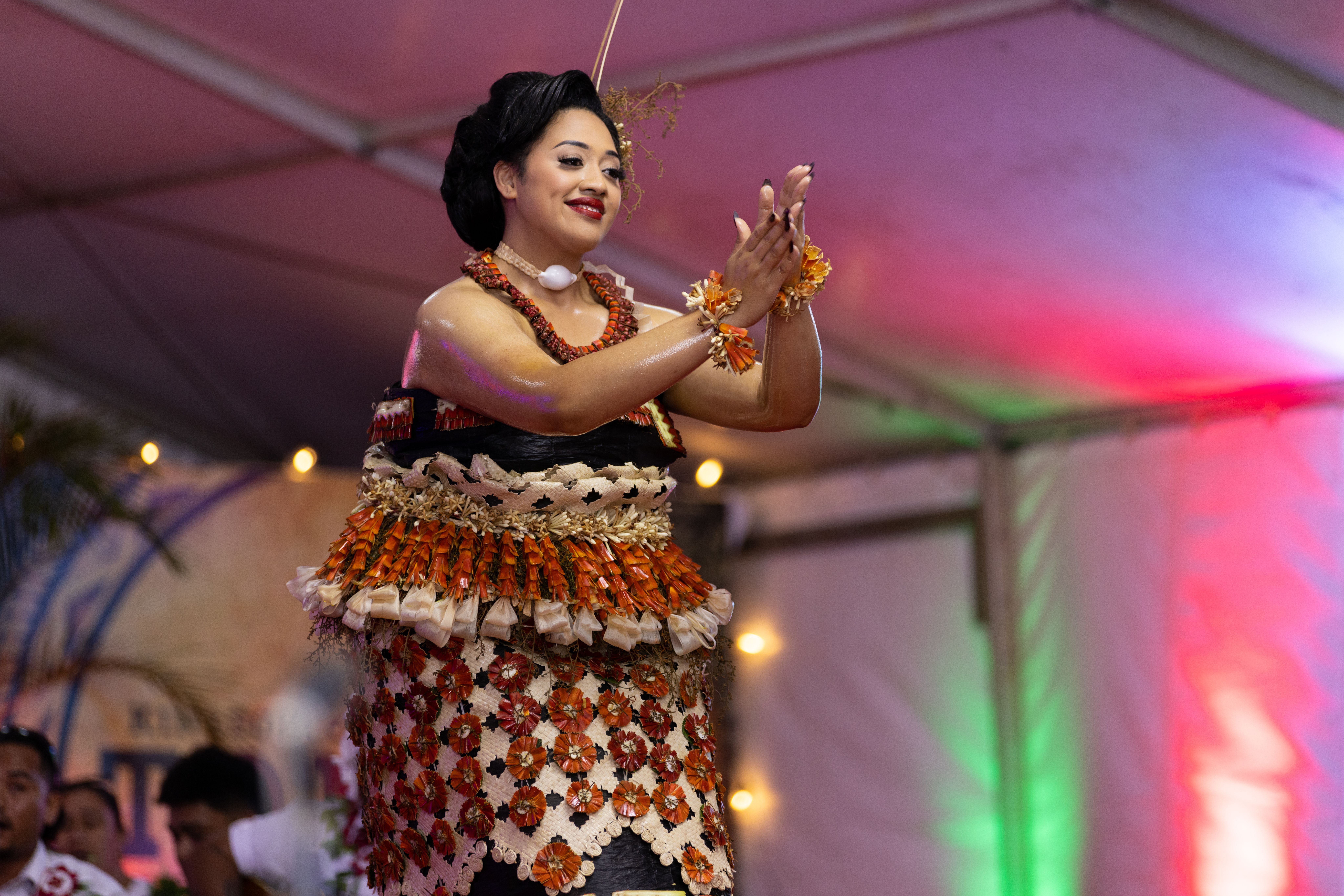 A performer in colourful traditional Polynesian attire performs an energetic Cook Islands dance accompanied by live drumming 