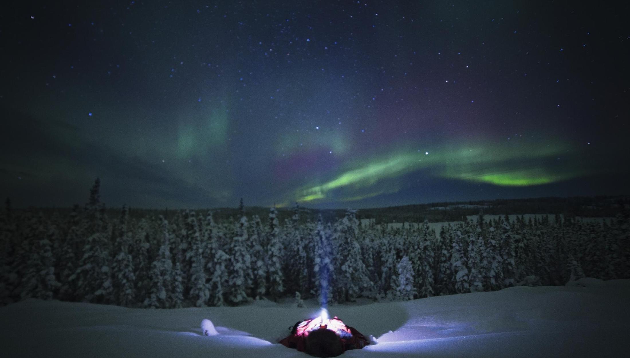 Person lying on ground and looking at the Aurora Borealis