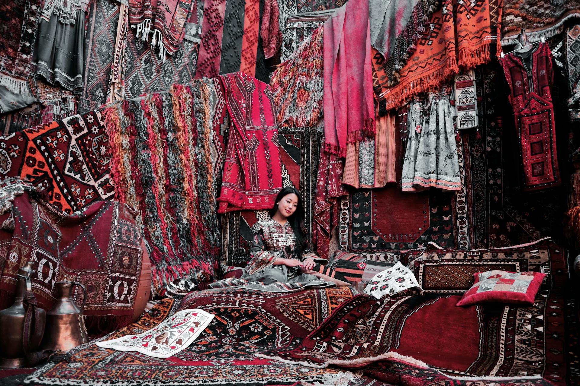 A woman sitting on a rug, surrounded by rugs draped around the walls