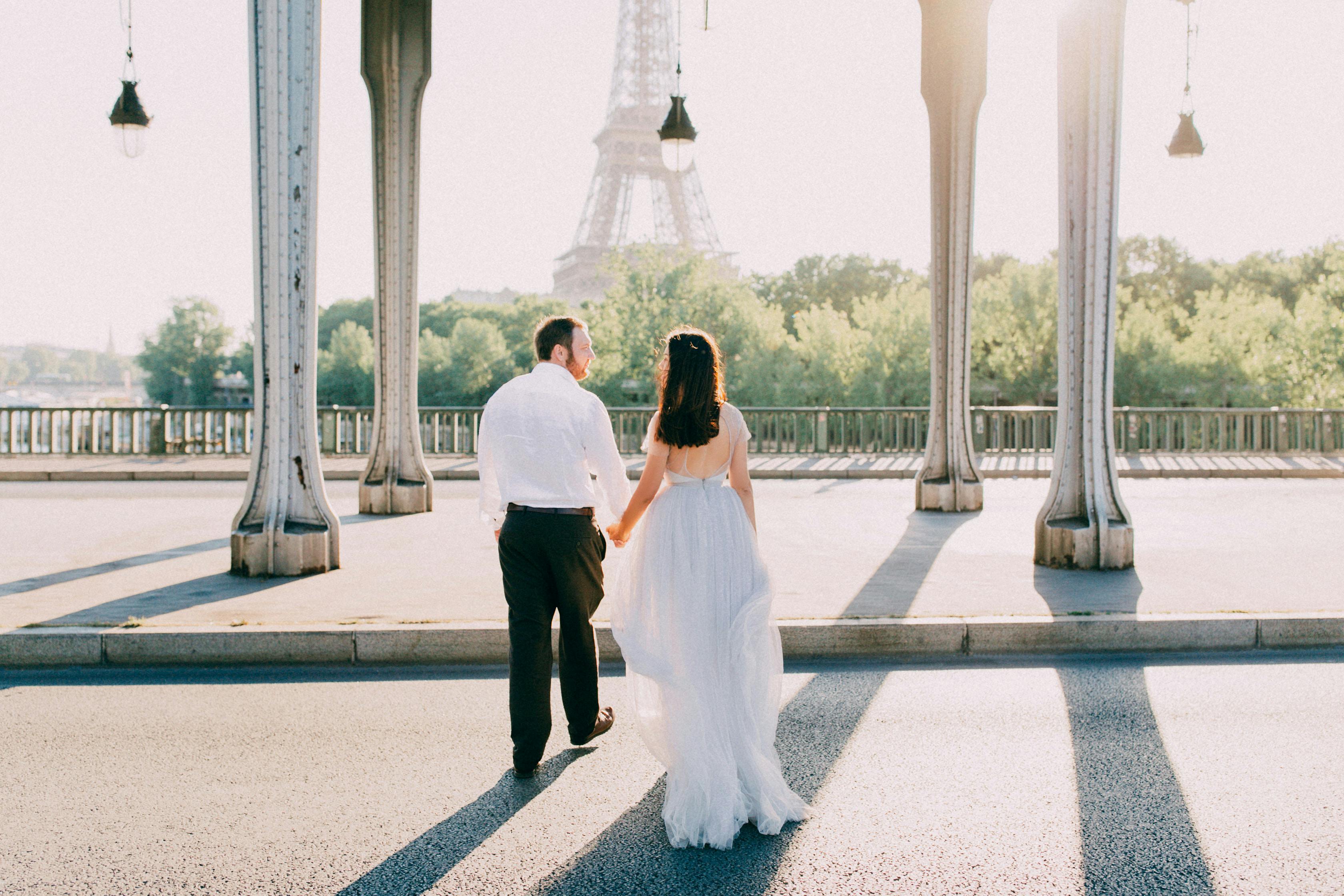 A man and woman holding hands while walking in the streets with the Eiffel Tower in the background