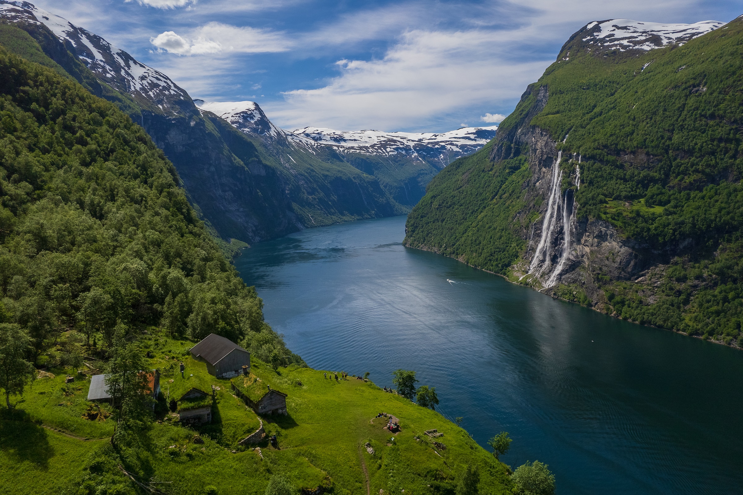The mighty Geirangerfjord runs through tall, steep mountains with lush greenery.