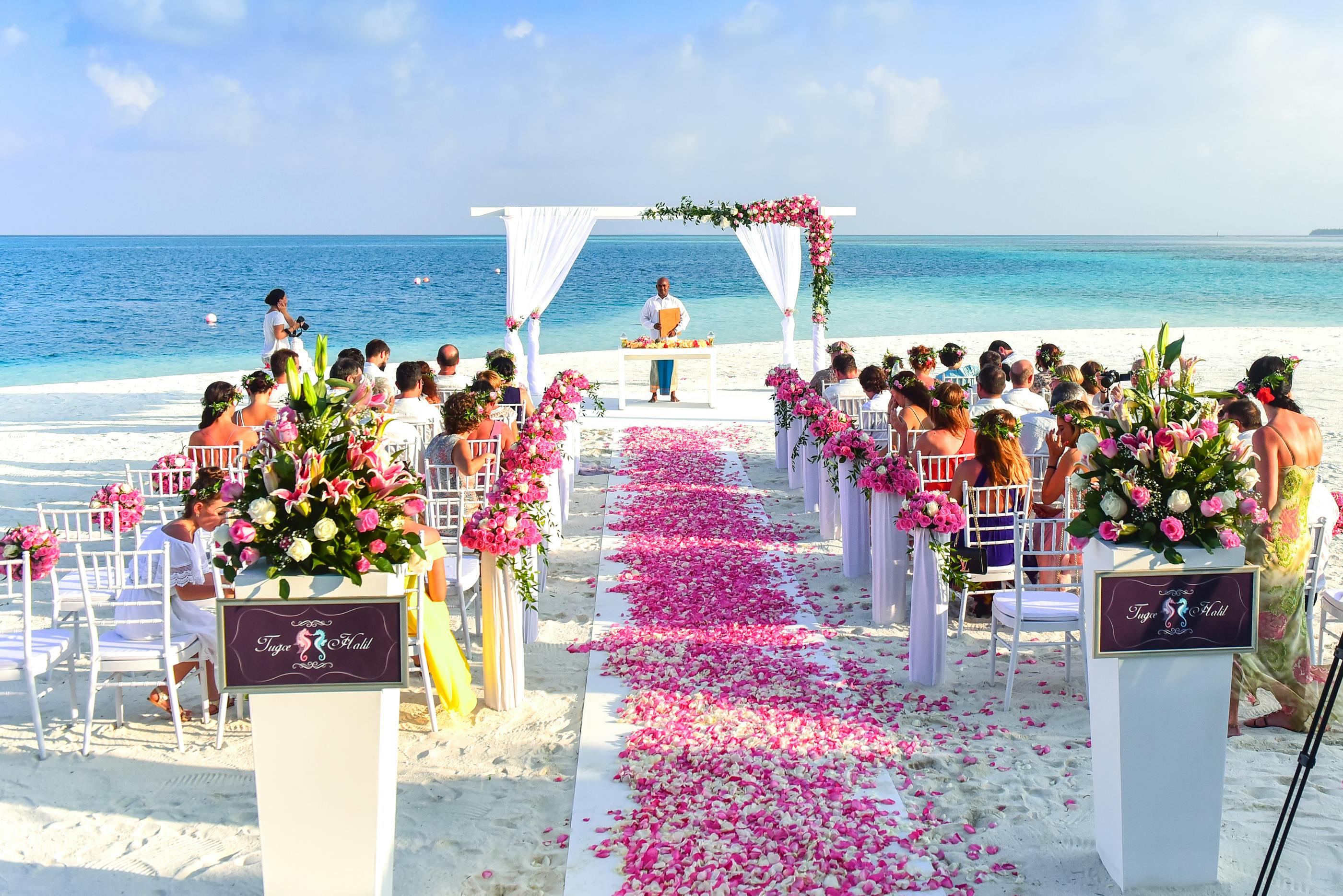 A wedding ceremony setup at a white-sand beach with plenty of pink flowers